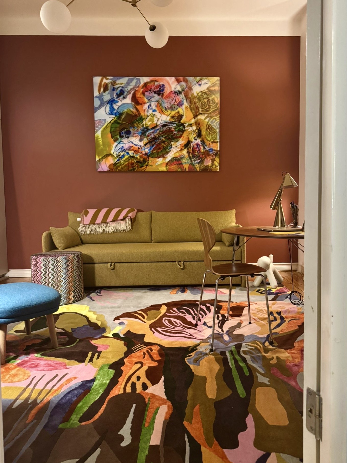 Private interior with the hand-woven carpet, olive sofa and a painting by Riitta Nelimarkka